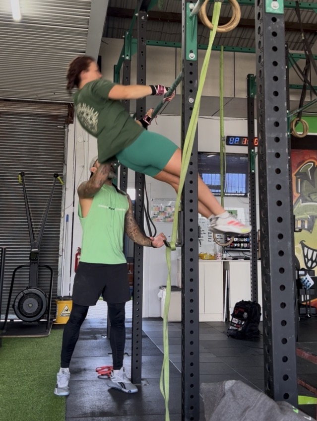 Jotik Serje assisting a client with a resistance band exercise on a gym rig