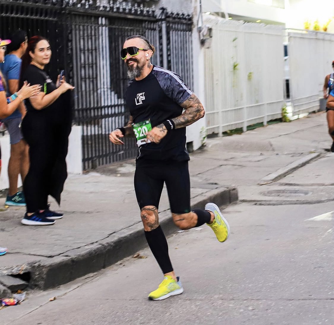Jotik Serje running in a road race, wearing a race bib and bright yellow shoes